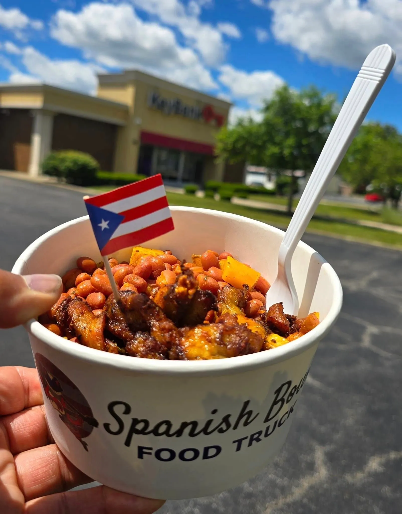 A person holding a cup of food with beans and meat.