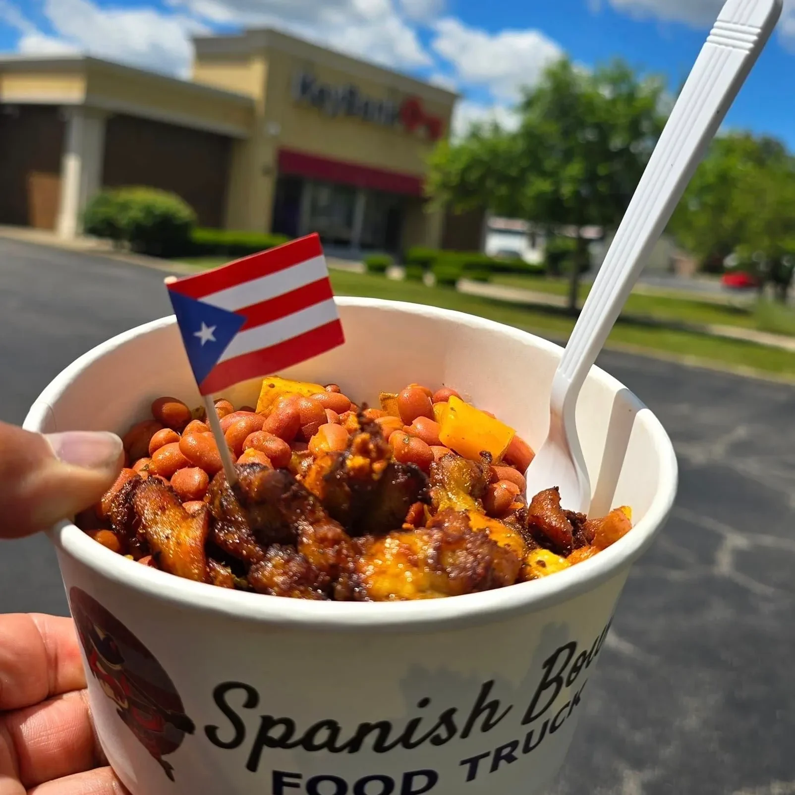 A person holding a cup of food with beans and meat.